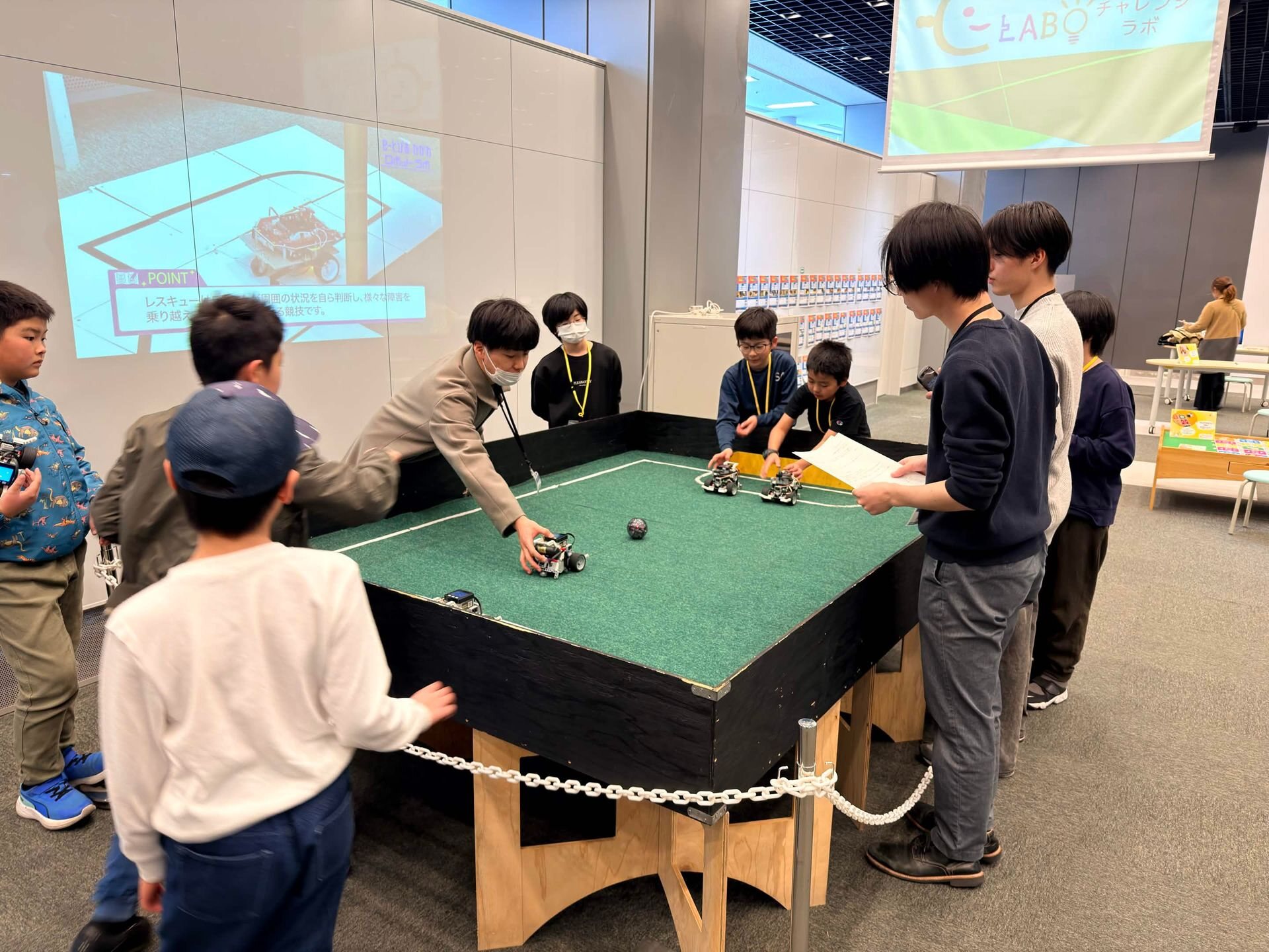 ロボット競技フィールドを囲み、子どもとスタッフが一緒にロボットを試している様子